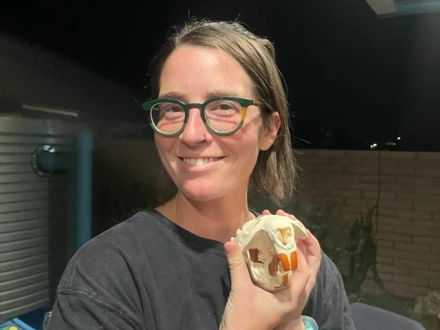 Bea Troxel, woman with brown hair tied up and round green glasses, holding a replica beaver skull