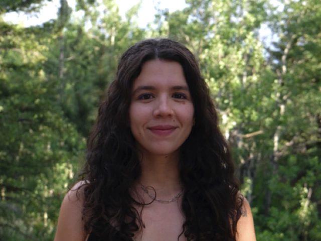Headshot of Isabel Gonzalez Mendez - a woman with long brown hair standing in front of greenery