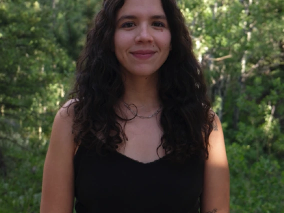 Headshot of Isabel Gonzalez Mendez - a woman with long brown hair standing in front of greenery