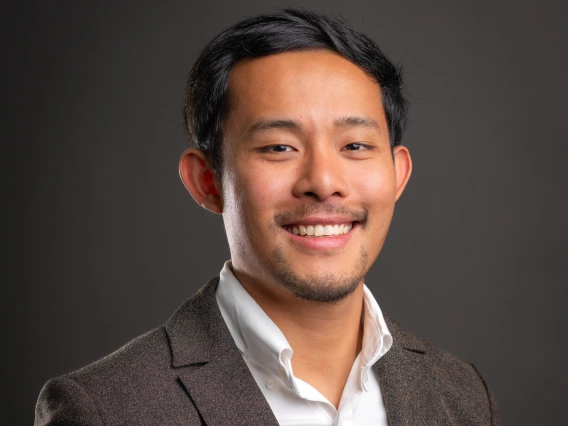 Mervin XuYang Lim - a man with short black hair and light facial hair smiling at the camera. He is wearing a white collared shirt and a brown jacket. 