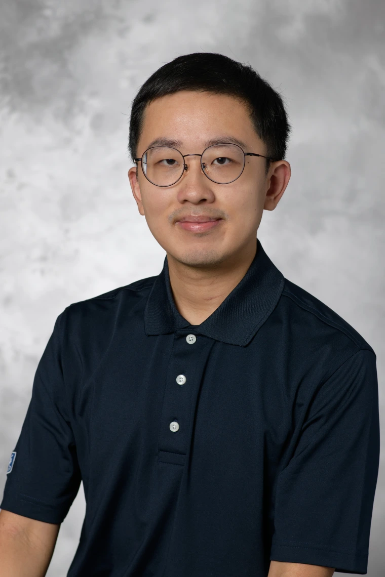 Beihua Guo - a man with short black hair and round glasses wearing a black polo shirt. Grey background