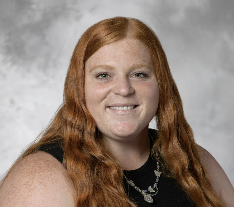 Headshot of Mikayla Deigan: woman with long, wavy red hair wearing a black tank top