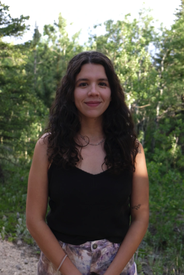 Headshot of Isabel Gonzalez Mendez - a woman with long brown hair standing in front of greenery