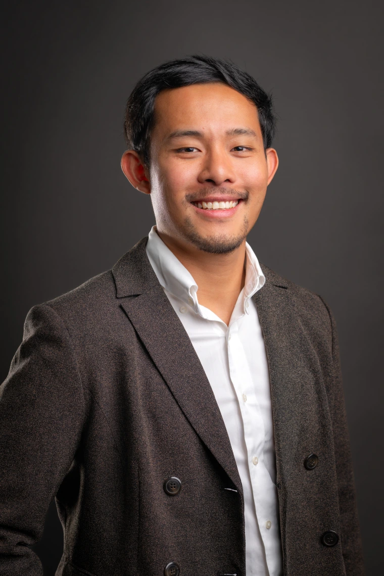 Mervin XuYang Lim - a man with short black hair and light facial hair smiling at the camera. He is wearing a white collared shirt and a brown jacket. 